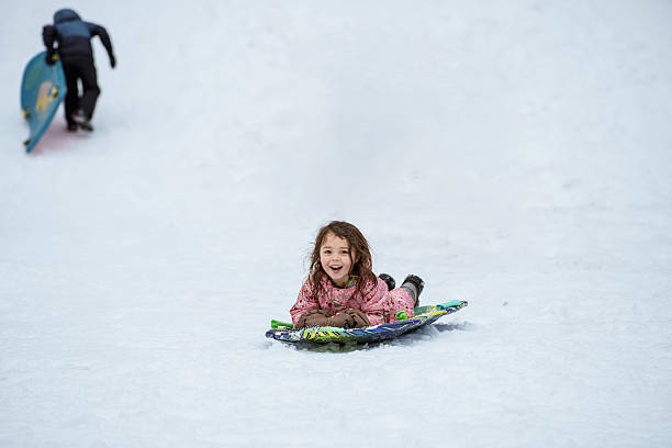 A five-year-old Eurasian girl smiles with excitement as she rides a snow sled down a hill during a fun winter day with her family at Mount Hood in Oregon, USA.