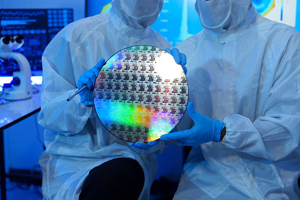 istock Engineers in sterile suits work at a semiconductor manufacturing plant using microscopes in a lab. 2242198439
