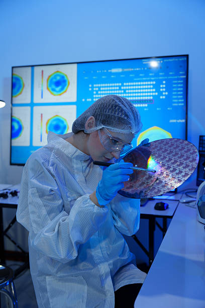 istock Engineers in sterile suits work at a semiconductor manufacturing plant using microscopes in a lab. 2242198489
