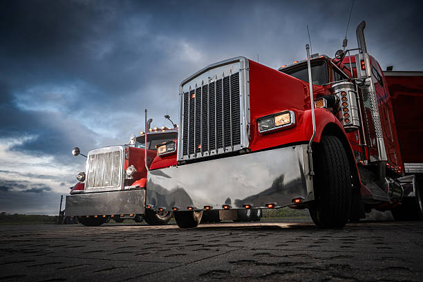 Two striking red trucks with shiny chrome accents are parked side by side against a dramatic twilight sky, capturing the essence of the trucking industry.