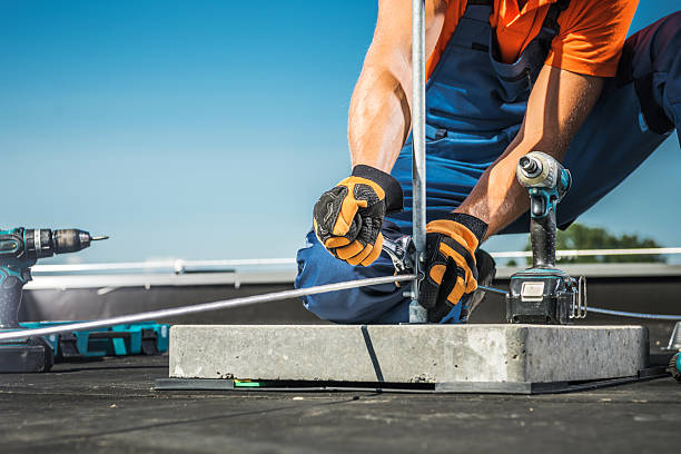 A skilled worker is securing a lightning protection rod to a concrete base on a rooftop. Thunderstorm building protection