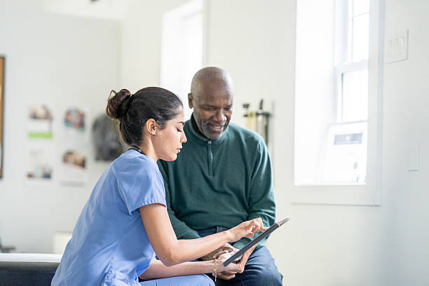 Hispanic Nurse Consults With Black Patient Using Tablet In Bright Clinic