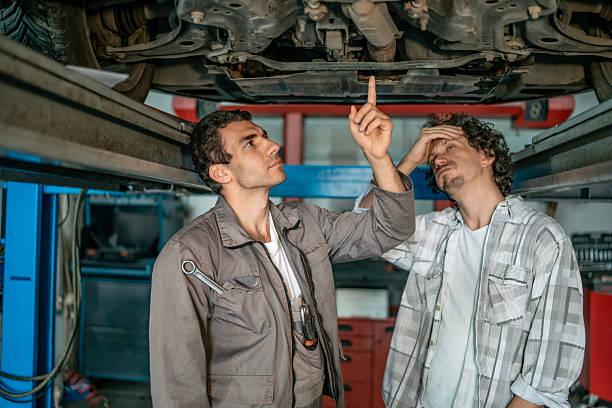 istock Two Mechanics Inspect Under a Car Lift, Discussing Repairs in a Busy Auto Workshop 2242211136