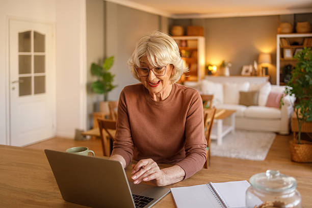 istock Cheerful senior woman using laptop for online therapy video call while sitting at desk in modern living room 2242212321