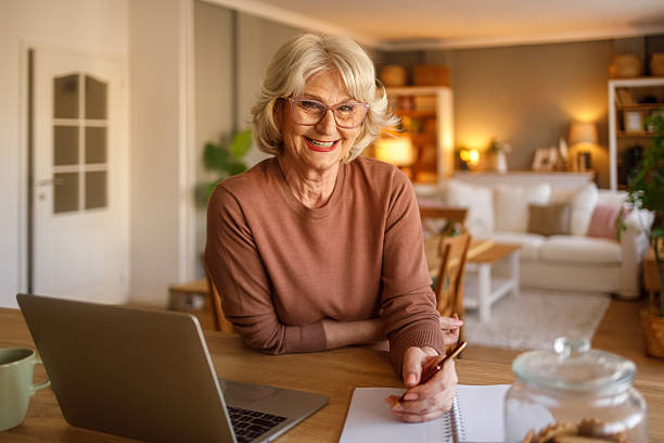 istock Portrait of smiling elderly woman writing expenses in notepad while using laptop for bill payments at home 2242212344