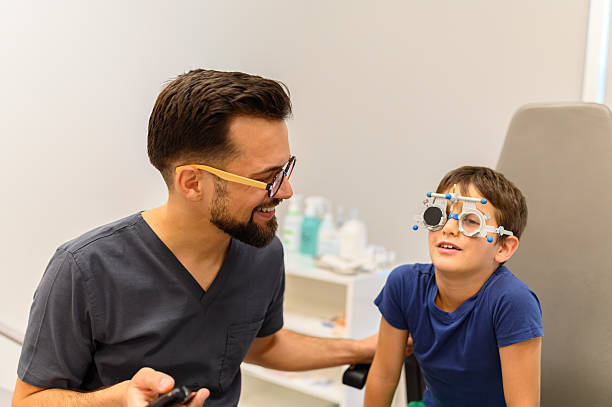 istock Boy wearing phoropter undergoing eye examination as male ophthalmologist operates remote control for vision test 2242212462