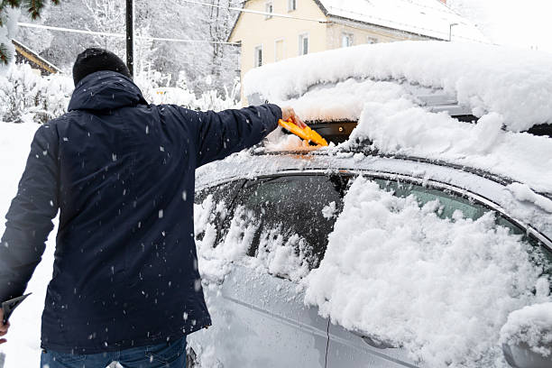 istock Man cleaning snow from a car during heavy snowfall in winter. 2242214025