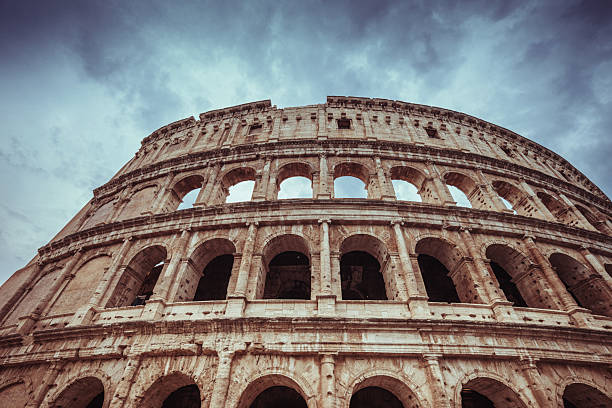 Majestic view of the Colosseum in Rome, Italy, captured from a low angle against a moody sky. The ancient amphitheater stands as an enduring symbol of Roman architecture, history, and grandeur.