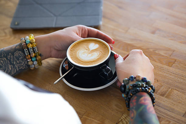 Stacked gemstone bracelets on tattooed wrists by a coffee table, colorful beads and ink