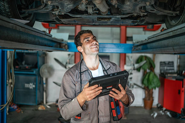 Mechanic Under Car On Lift Inspecting With Tablet Diagnostic Tool In Auto Shop