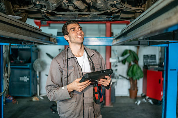 istock Mechanic Using Diagnostic Tool Under Car On Lift In Auto Shop 2242223631