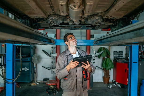 istock Mechanic Using Tablet Diagnostic Tool Under Car On Lift In Auto Repair Shop 2242223640