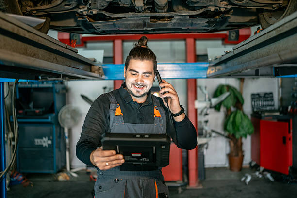 istock Happy Auto Technician Using Tablet and Phone in Busy Garage Under Car Lift 2242223782