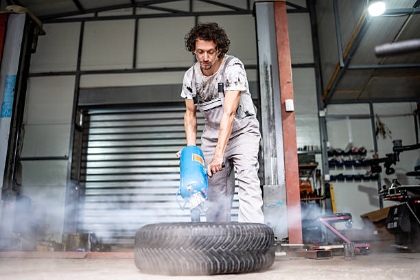 Worker Using Spray Device On Tire In Workshop Creating Smoke In Industrial Garage