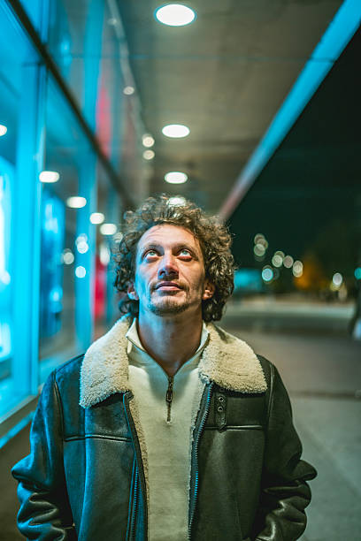 istock Man In Leather Jacket Gazing Upward Under Blue Neon Lights At Night 2242224458