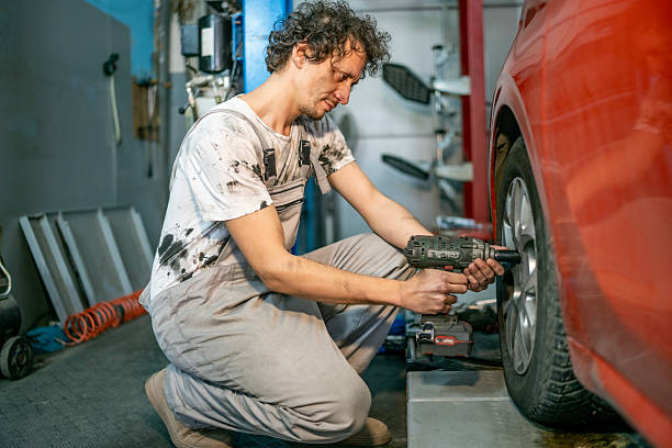 istock Mechanic Repairing Car Tire Using Drill In Auto Shop While Kneeling Beside Wheel 2242224504