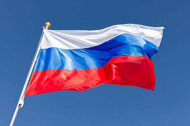 istock A vivid Russian flag flutters atop a tall pole, set against a clear blue sky 2242227567