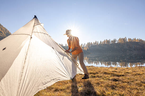 istock Sunset Camp: Woman Setting Up Tent by the Mountains 2242231841