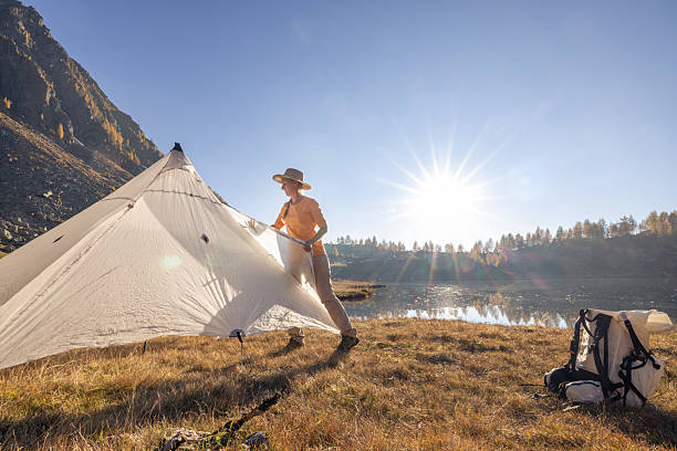 istock Woman Setting Up Tent by Mountain Lake 2242231910