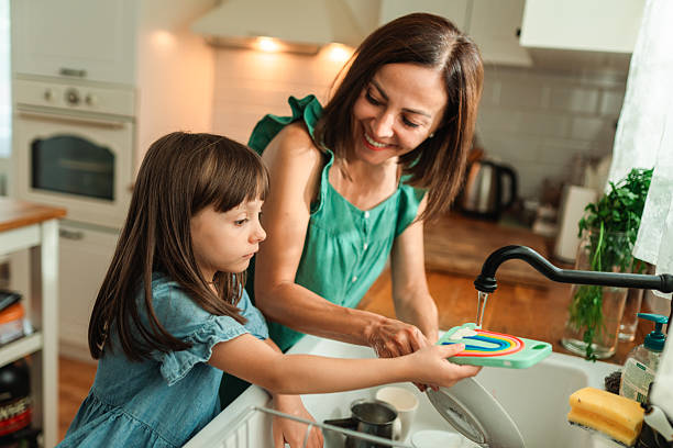 istock Mother teaching daughter to wash dishes at kitchen sink 2242233572