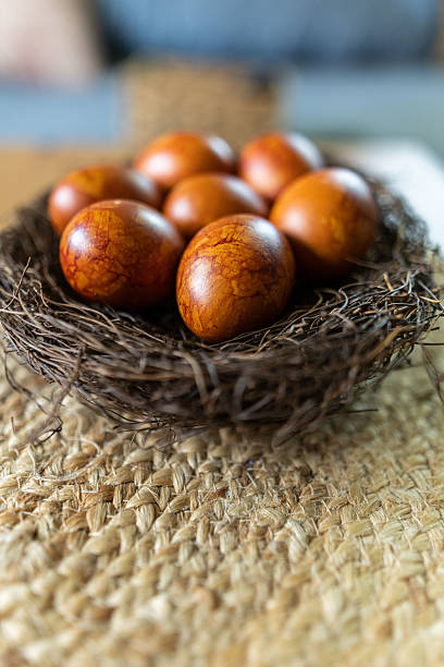 Close-up of naturally dyed Easter eggs in warm brown and orange tones, placed in a rustic nest. The eggs are decorated using traditional onion skin dyeing technique, symbolizing heritage, culture, and festive spring celebrations. Perfect for themes of Easter, tradition, and organic natural food styling.
