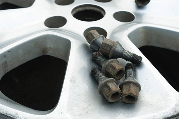 Rusty lug bolts lying on a silver alloy car wheel, representing auto maintenance