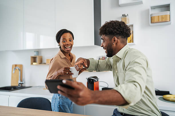 istock Diverse couple enjoying morning coffee laughing with tablet 2242240828