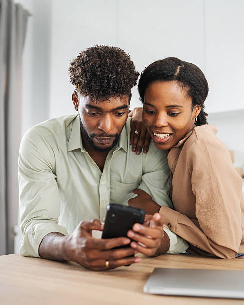 istock Young black couple sharing content on smart phone in kitchen 2242240947
