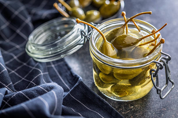 istock Pickled capers berries in jar on black table. 2242241089