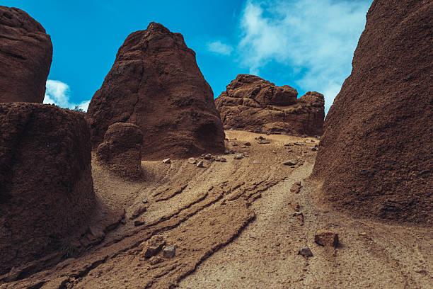 Eroded volcanic rock formations rising from the arid landscape of Tenerife under a partly cloudy sky. The natural textures and sculpted shapes reveal the island’s dramatic geological past.
