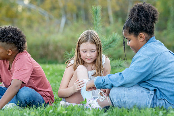 istock Three Diverse Kids Sharing a Moment Outdoors: Friends Helping Each Other Sit on Grass in a Park 2242270426