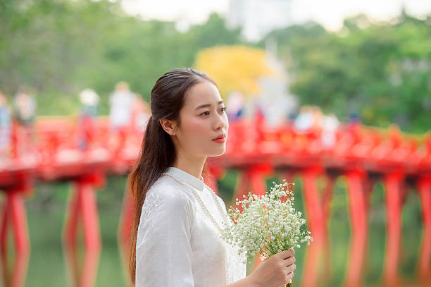 A Vietnamese woman in a traditional white dress at a landmark in Hanoi, the capital of Vietnam.