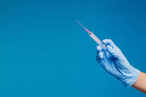 istock Medical hand holding syringe with pink needle on blue background. 2242295026