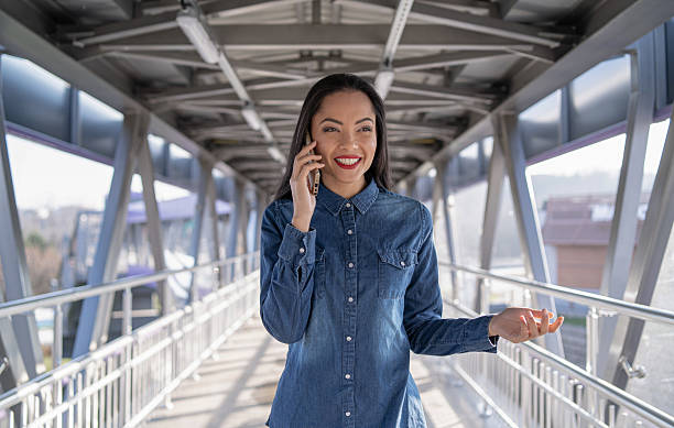 istock Young woman confidently chatting on her phone while walking along a modern urban bridge. 2242295099