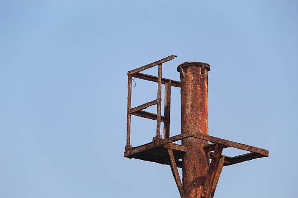Close-up of an old rusty metal pole structure against clear blue sky. Industrial decay, weathered steel, and minimal composition showing texture, corrosion, and aging over time in outdoor environment