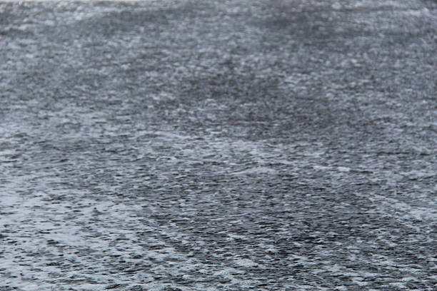 Close-up of water surface during rainfall with ripples and splashes. Ideal for nature, texture, or weather-themed visual content