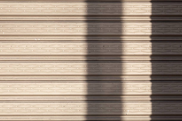 Gray corrugated metal door with abstract shadows cast by natural light, creating a modern industrial background suitable for design, construction, and architectural projects.