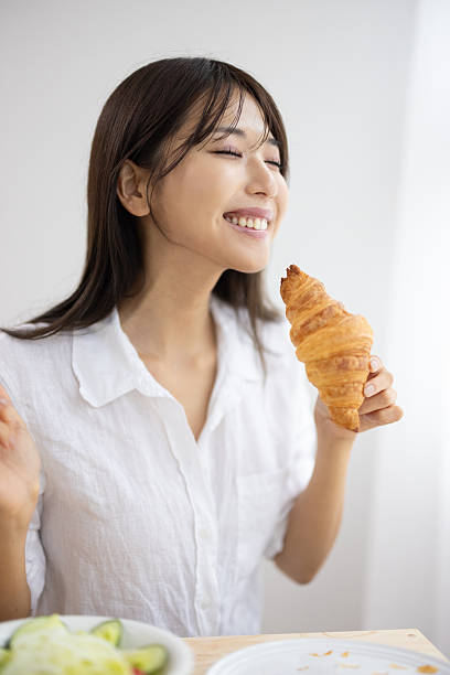 Smiling Young Woman Enjoying a Croissant for Breakfast