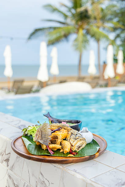 Crispy fried fish on plate by poolside tropical resort, palm trees,