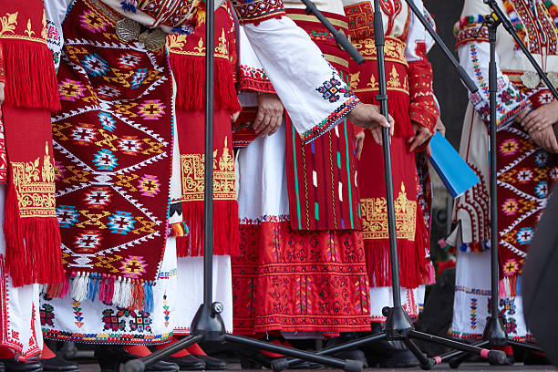 The Bulgarian national costume displays vivid red and white colors, rich embroidery, and traditional accessories, representing cultural heritage and craftsmanship in a lively performance atmosphere
