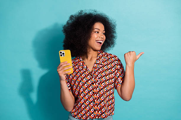 istock Young woman with colorful patterned shirt smiles while using a yellow smartphone against a blue background 2242323702
