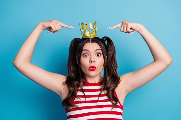 istock Cheerful young woman wearing a crown, gesturing fun expressions while posing against a vibrant blue background 2242325259
