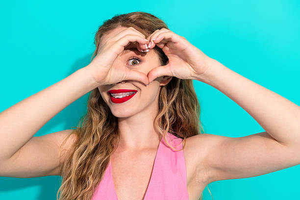 istock Young woman forms a heart frame with her hands smiling brightly against a turquoise backdrop for fashion lifestyle and fun stock photo 2242326595