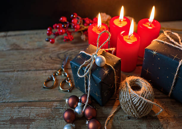 Eco-friendly holiday wrapping with twine, recycled paper, and natural materials surrounded by red candles and ornaments. The warm light and rustic wood background emphasize sustainability and the emotional warmth of giving mindfully. Copy space for text - Christmas, backgrounds