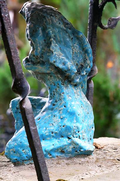 A very weathered abstract blue stone sculpture in a cemetery.
