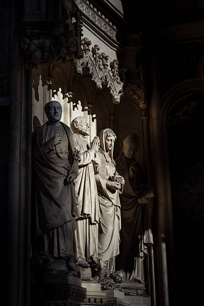 Detailed stone sculptures of religious figures in gothic-style church, partially lit by natural light, conveying solemnity and reverence.