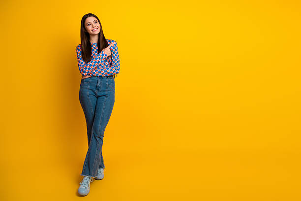 istock Young woman stands against a bright yellow background wearing jeans and a patterned top smiling with arms crossed in a casual chic lifestyle portrait 2242328355