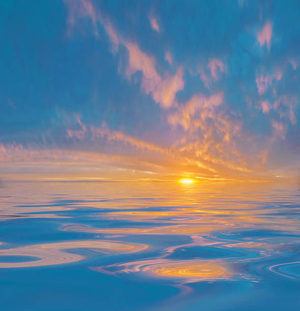 A vivid sunrise or sunset illuminates tranquil water as warm-toned clouds scatter across the deep blue sky