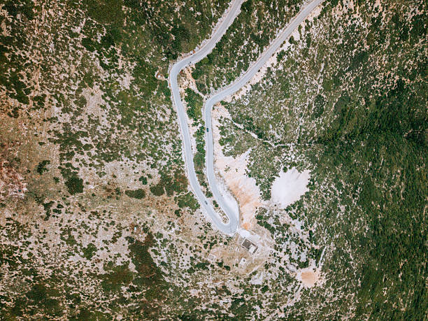 Aerial view of a winding mountain road with one car driving through rocky terrain. Remote landscape with sparse vegetation and rugged hills. Mountain road travel and nature scenery.