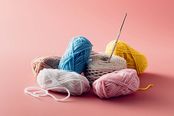 A vibrant collection of yarn balls in pastel colors with a needle on a soft pink background, ideal for crafting, creativity, and DIY projects.